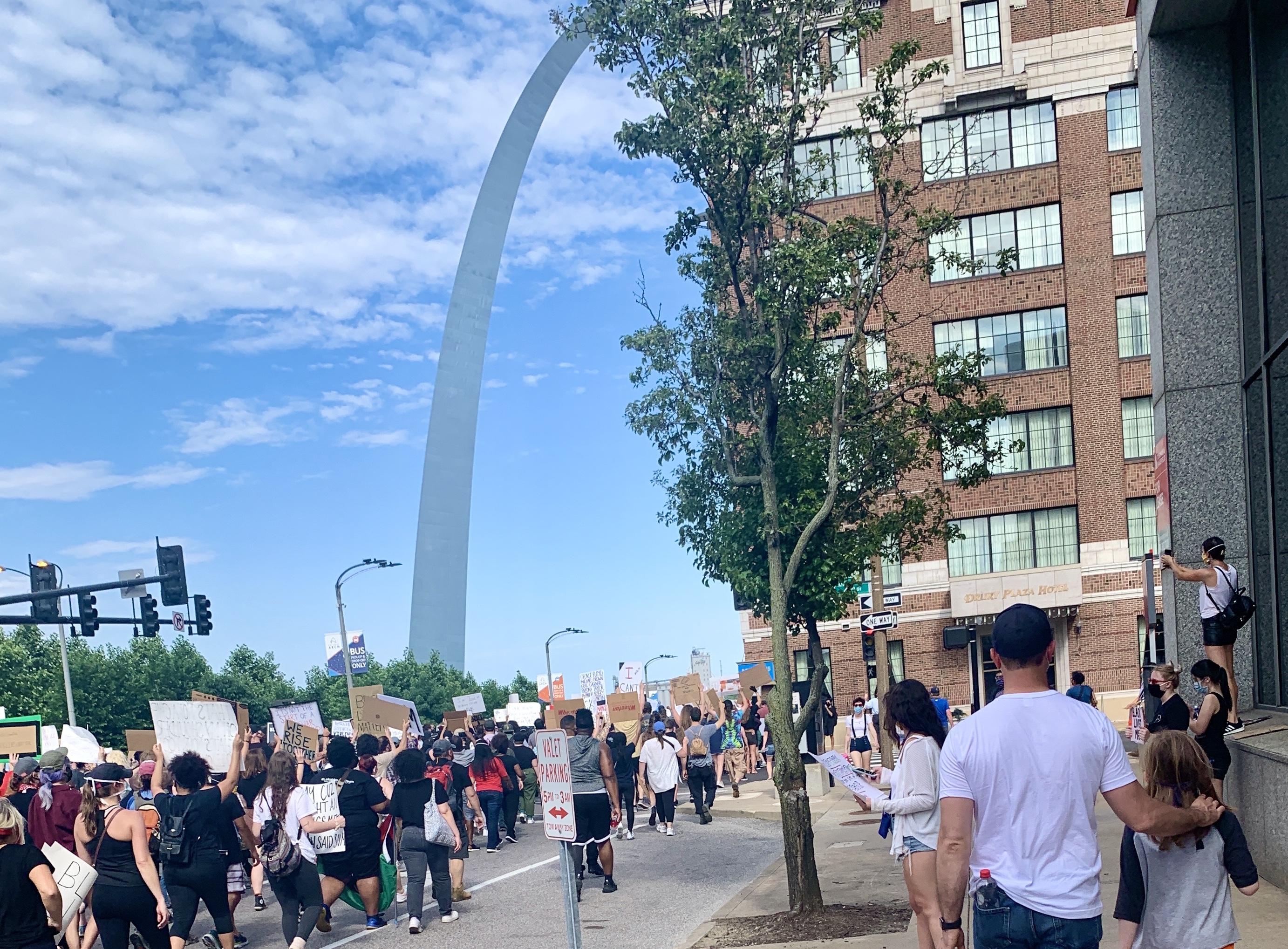 Groups of people walk in unison marching with the Gateway Arch in the background